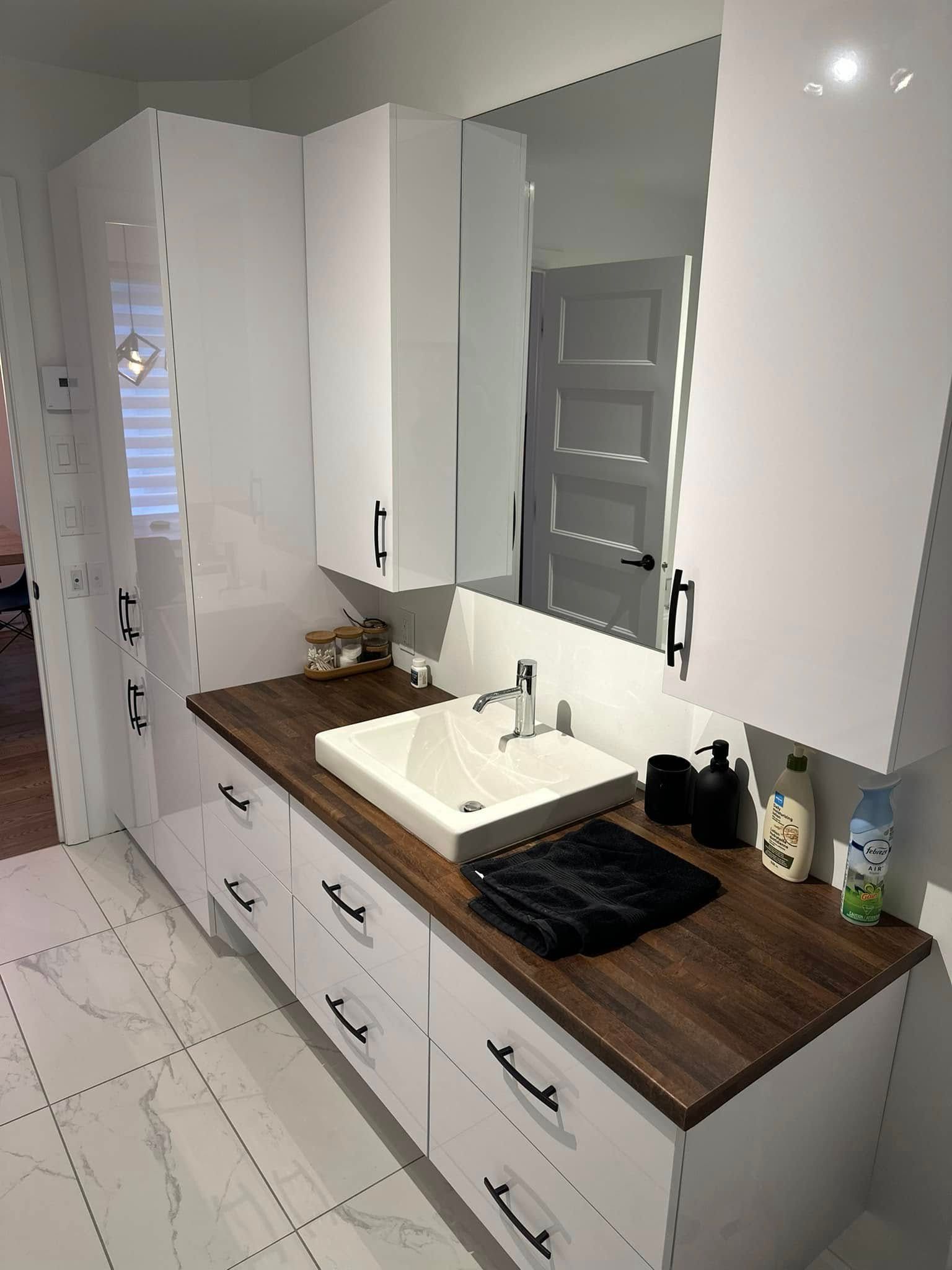 Meuble-lavabo moderne avec armoires blanches, comptoir en bois foncé, vasque rectangulaire blanche et grand miroir mural.