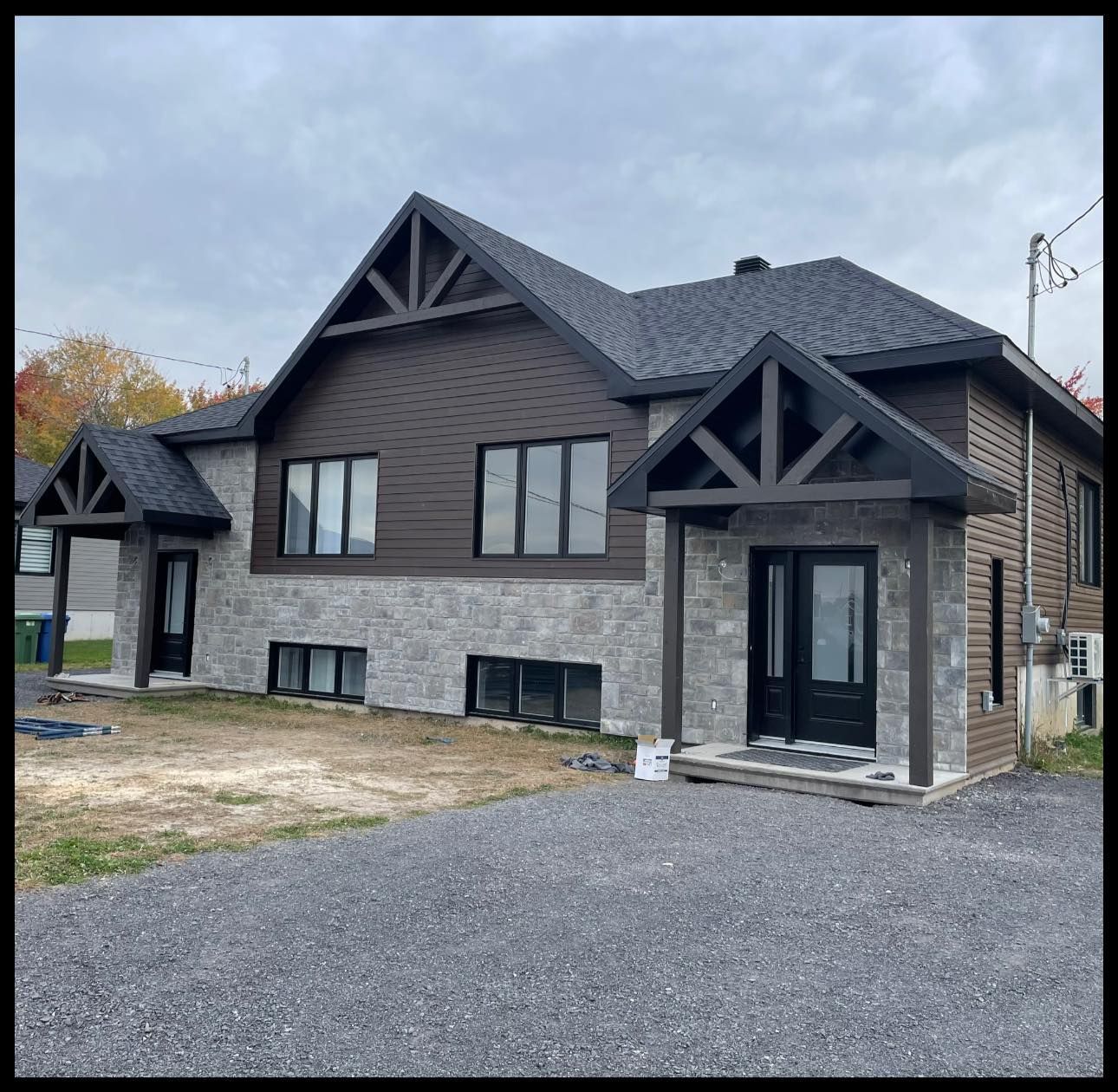 Une maison moderne à deux étages avec un revêtement en pierre grise au rez-de-chaussée, un revêtement horizontal brun à l'étage et des finitions noires.