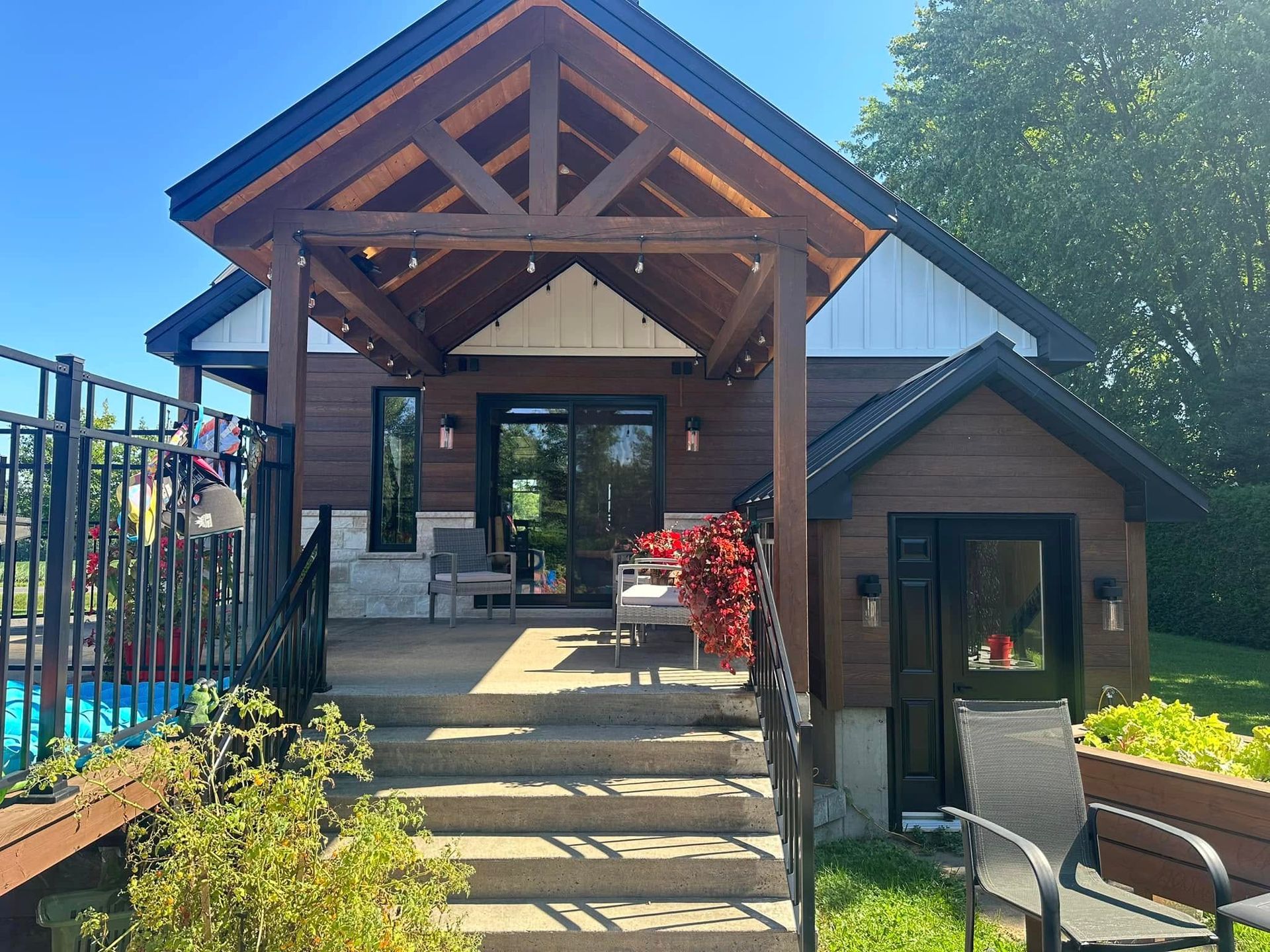 Un chalet moderne avec une véranda à ossature bois, des marches en béton et une entrée latérale séparée, situé à côté d'une piscine.