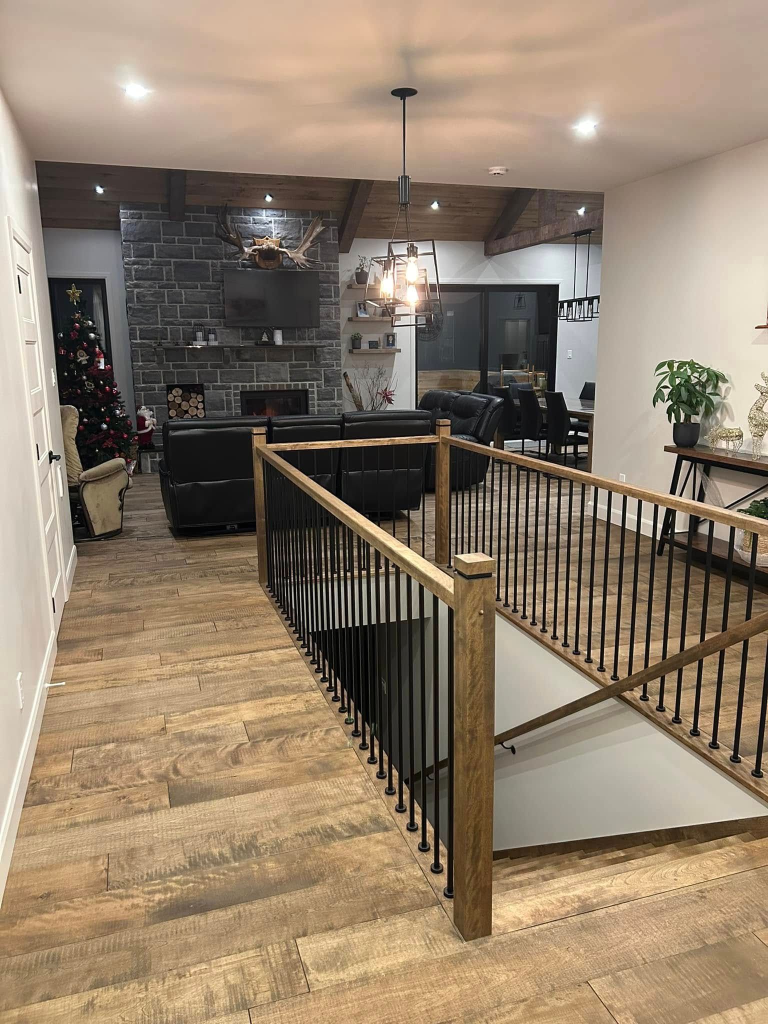 Un salon de style rustique comprend une cheminée en pierre, un parquet, une rampe d'escalier et une vue sur la salle à manger.