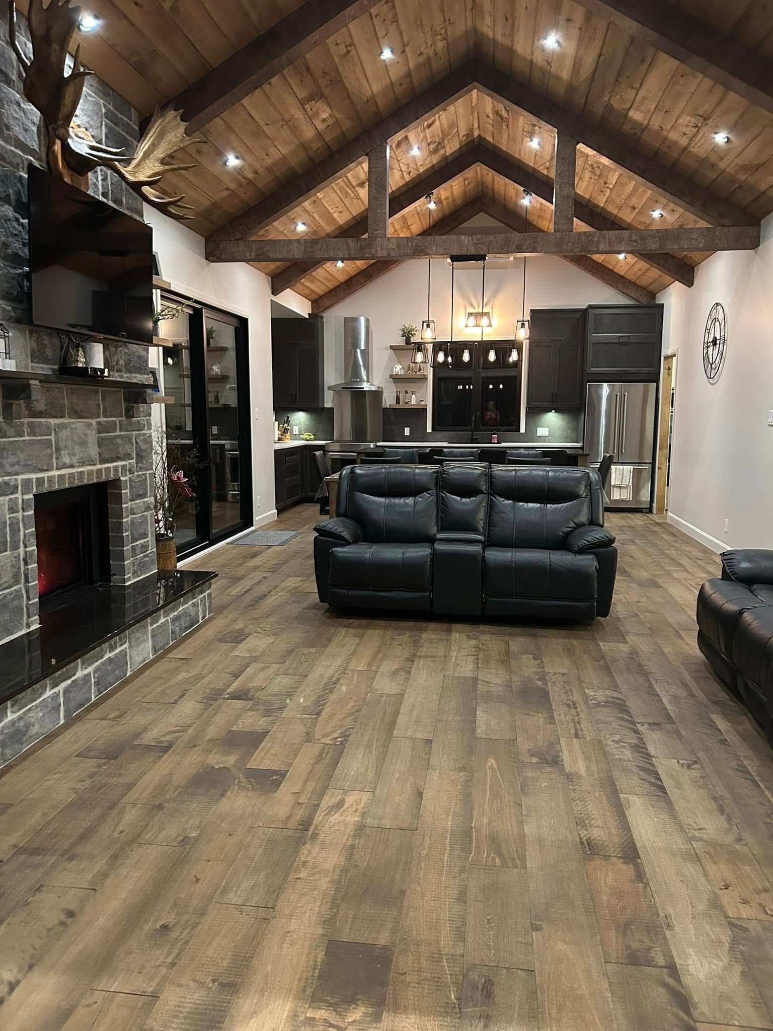 Espace de vie rustique à aire ouverte avec plafond voûté lambrissé, cheminée en pierre et meubles en cuir noir.
