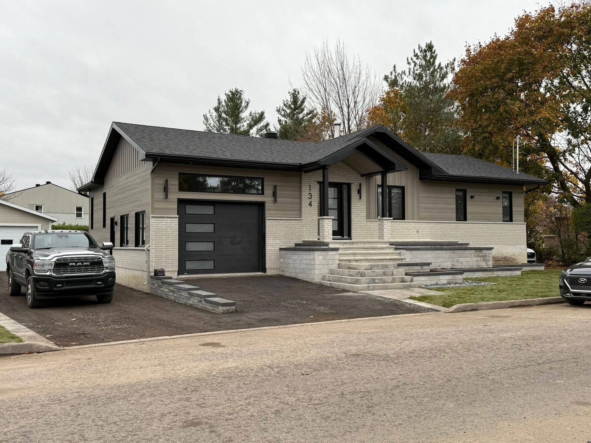 Maison de plain-pied avec bardage horizontal, éléments en pierre, porte de garage foncée et marches menant à l'entrée principale.