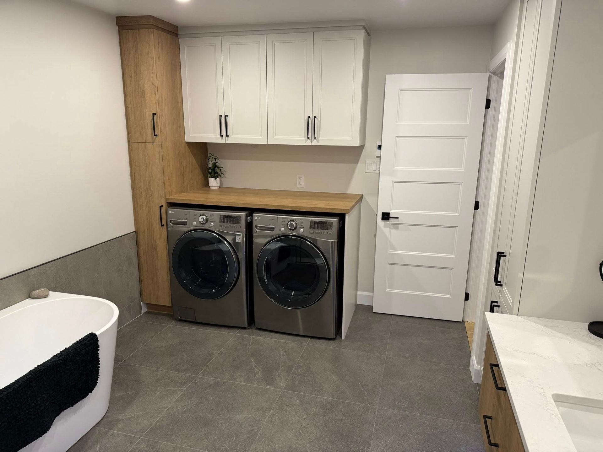 Une buanderie comprenant une machine à laver et un sèche-linge sous un plan de travail en bois, des placards hauts blancs et une haute armoire en bois.