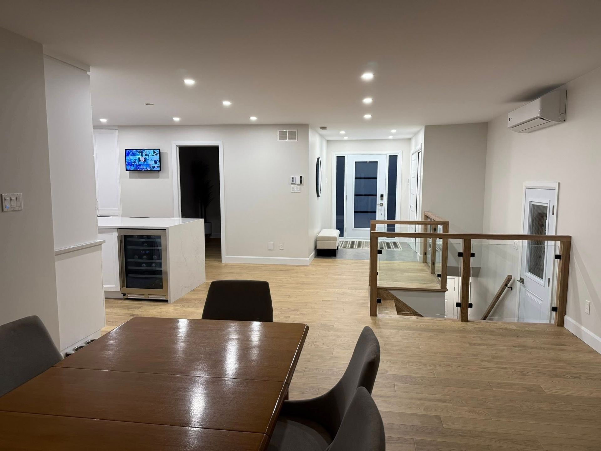 Un espace de vie moderne et ouvert avec parquet clair, une table à manger, une cave à vin et un escalier avec rampe en verre.
