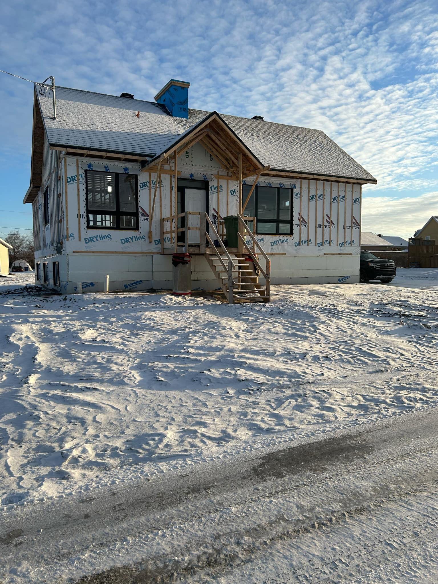 Une maison en construction dans un champ enneigé, avec un bardage blanc, une entrée en pente et des fenêtres sombres.