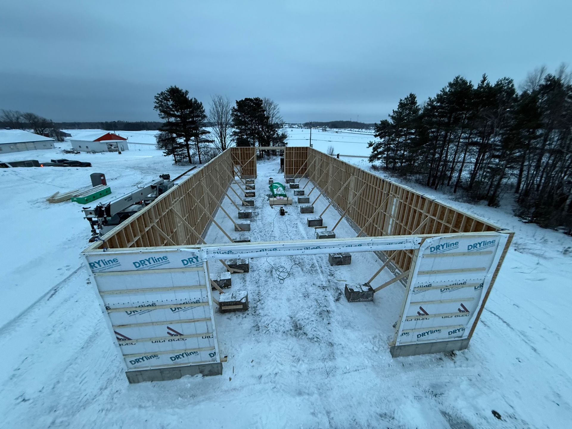 Vue aérienne et panoramique de la charpente en bois d'un bâtiment en construction, entourée d'un paysage enneigé.