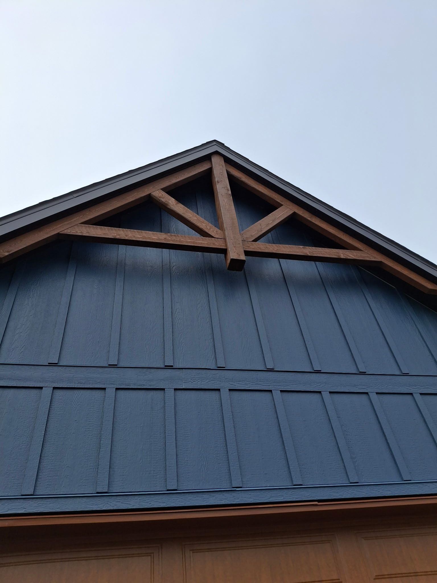 Un pignon bleu à panneaux verticaux, orné d'une ferme décorative en bois brun, se détache sur un ciel dégagé.