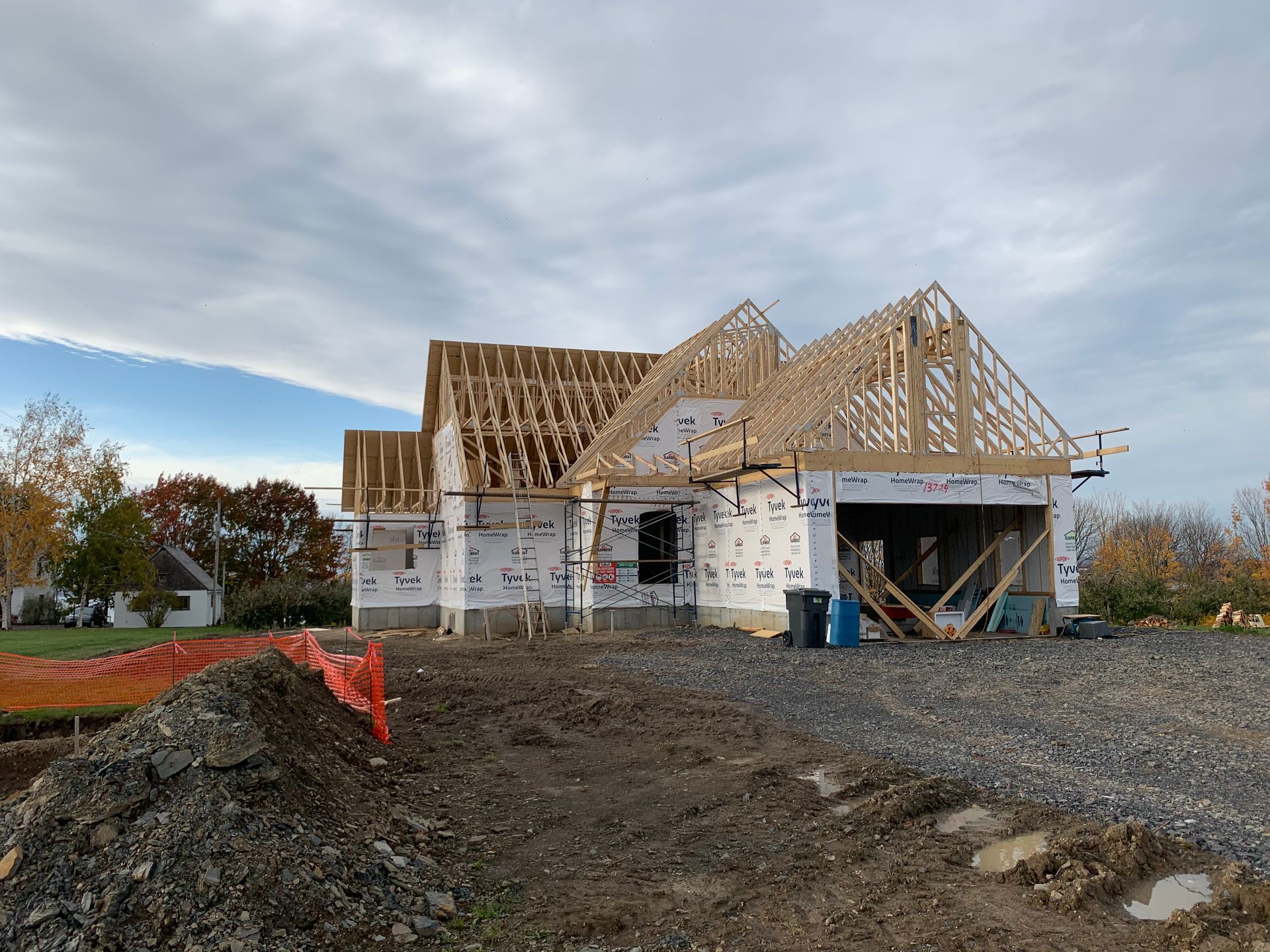 Une maison en construction, avec sa charpente apparente en bois et son pare-vapeur blanc, par temps couvert.