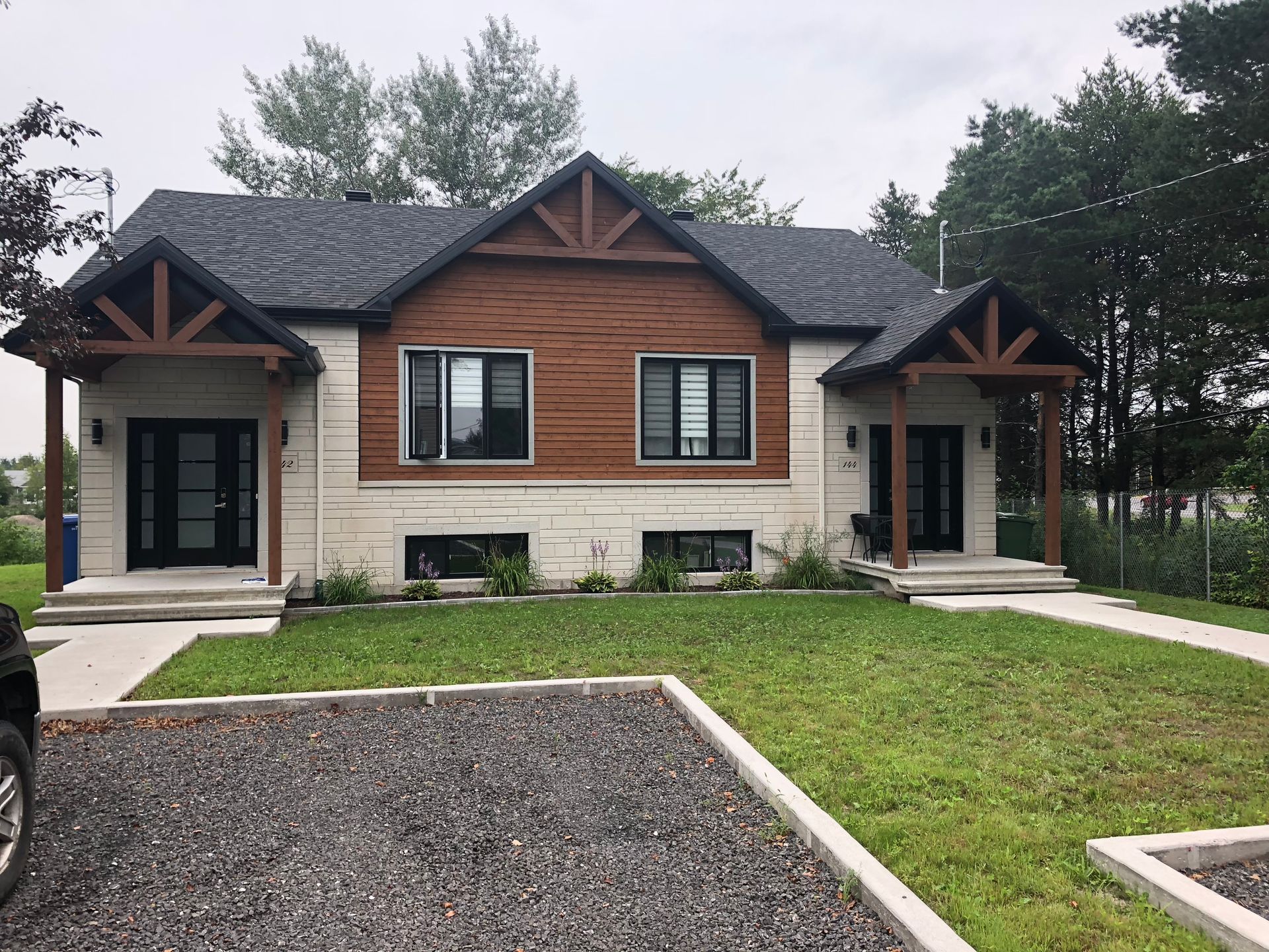 Un duplex moderne avec un revêtement extérieur en pierre blanche et en panneaux de bois, doté de deux entrées symétriques avec des accents de bois foncé.