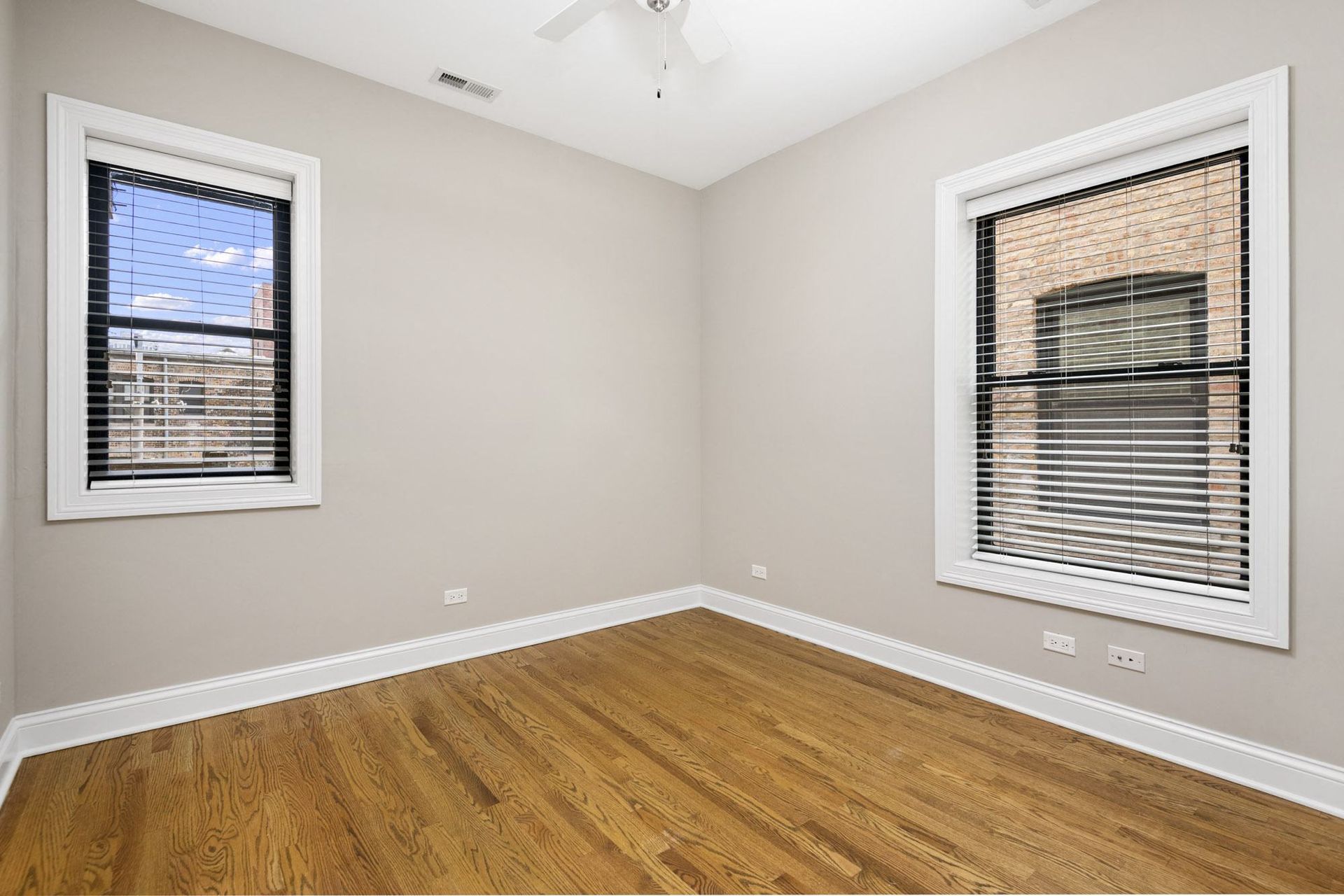 an empty room with two windows and wood floors