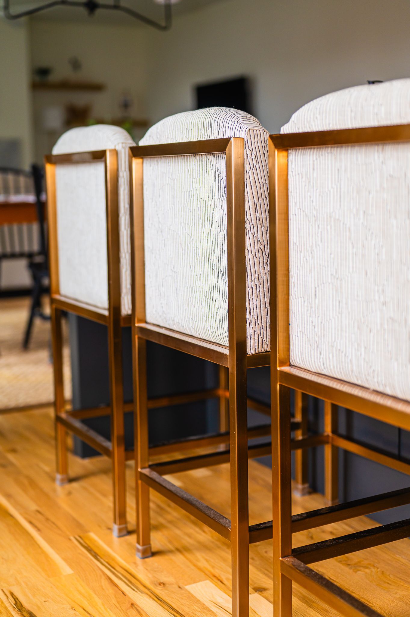 Close-up of brass bar stools with light patterned backs and seats at a kitchen island.