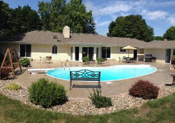 Backyard patio with a curved swimming pool, lounge chairs, and a house in the background