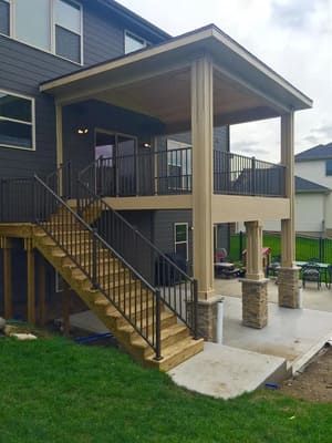 Covered outdoor staircase and patio beside a dark-sided house with black railings and concrete steps.