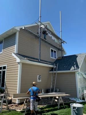 Workers on scaffolding painting the exterior of a beige house on a sunny day