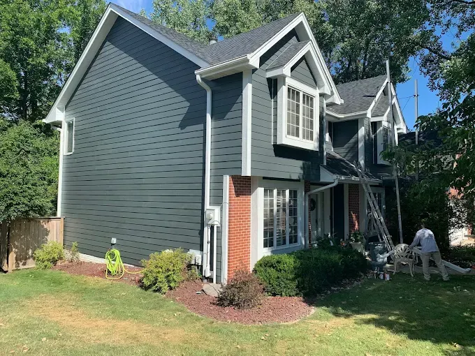Blue-gray house with white trim, red front accent, and a small lawn in a leafy suburban yard