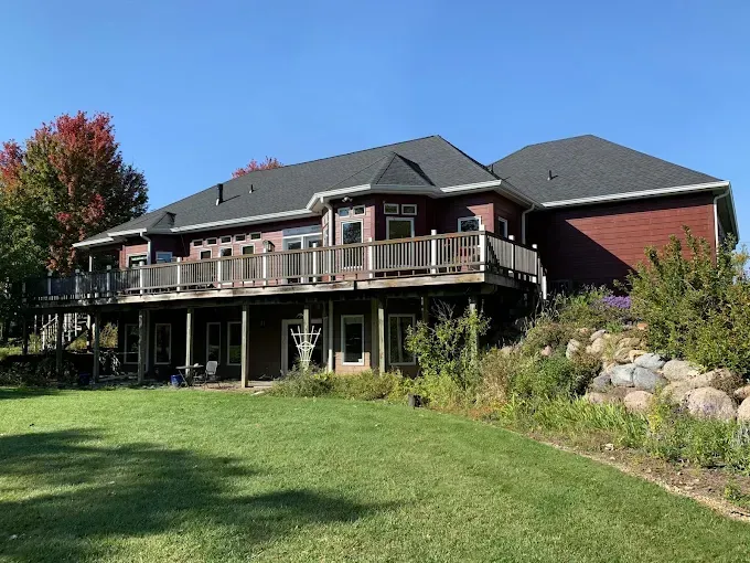 Suburban house with a large wooden deck overlooking a green lawn and landscaped yard