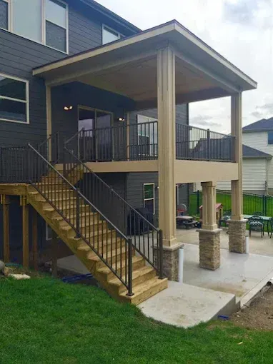 Covered wooden staircase and balcony attached to a dark-sided house, with concrete patio and grass yard