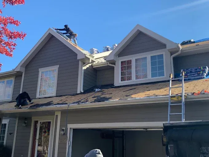 Roofing work on a gray house with workers on the roof and a ladder at the front porch