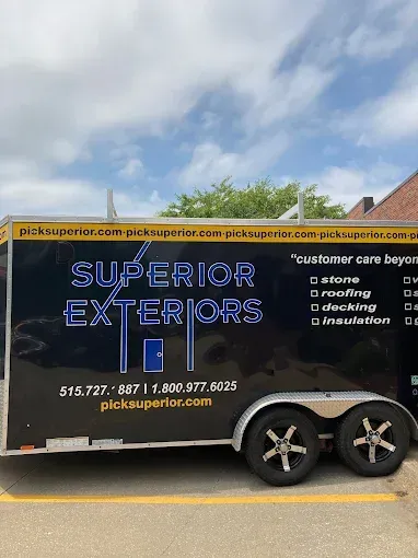 Black Superior Exteriors work trailer with service list and contact info on a road under a cloudy sky