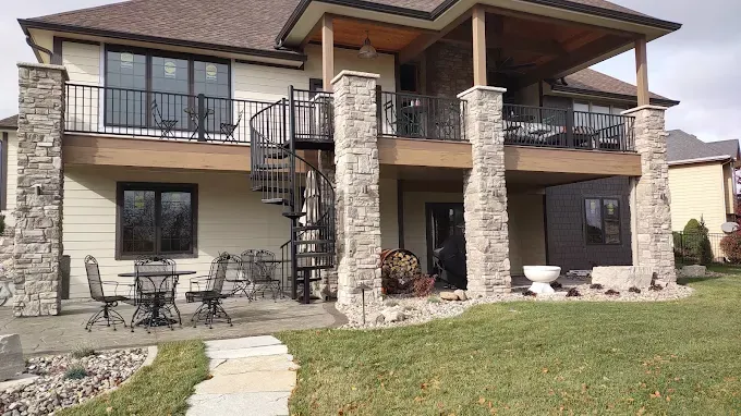 Two-story house exterior with stone columns, balcony, and front lawn
