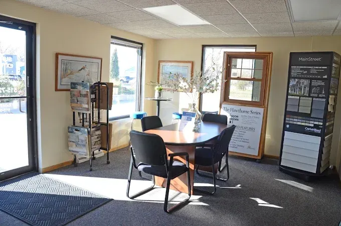 Waiting area with round table, chairs, brochures, and display stands in a sunlit office lobby