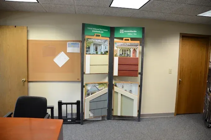 Office hallway with a display of glass panels, bulletin board, desk, and doors under fluorescent lights
