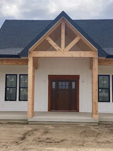 Front view of a new house entrance with white siding, wood trim, and a covered porch under a cloudy sky