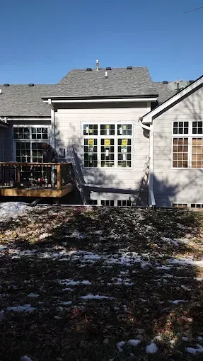 House exterior with white siding, central glass doors, and a small deck in a snowy yard.
