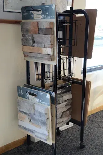 Rotating display rack with hanging wood and metal sample boards in a carpeted room near a window