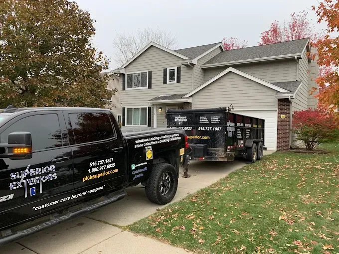 Black truck and trailer parked in front of a gray house with autumn trees and lawn signs
