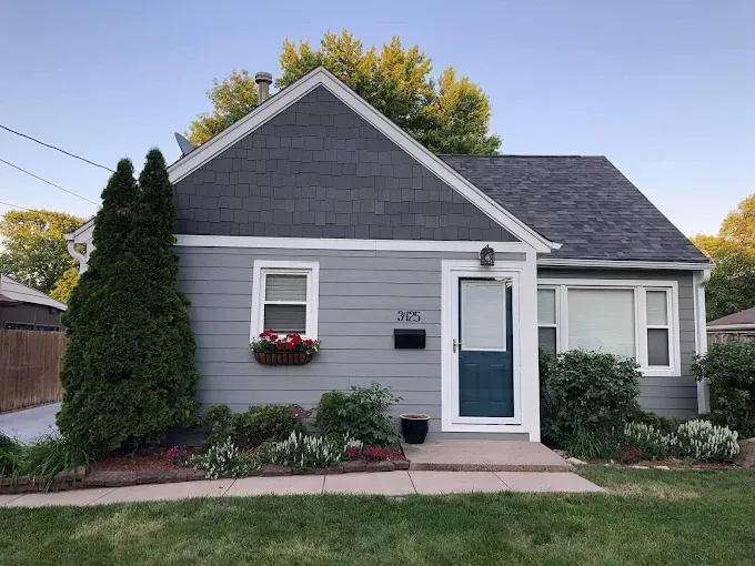 Small gray house with blue front door, white trim, and a flower box by the window.