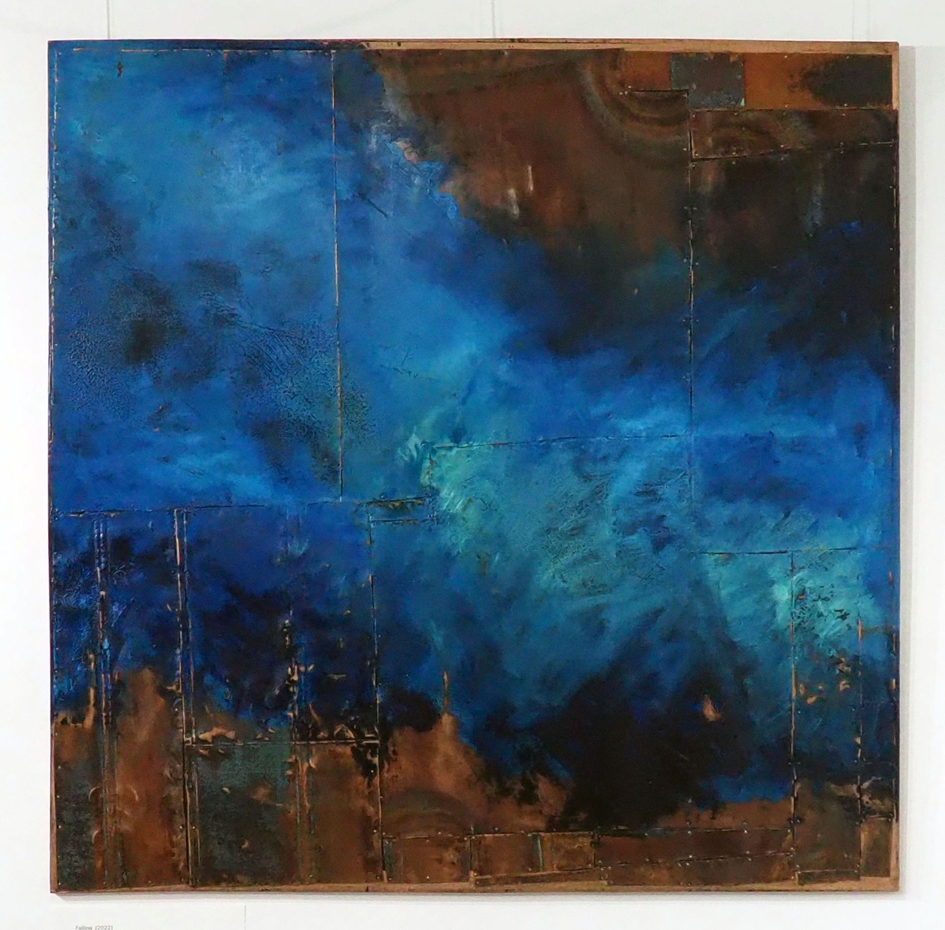 Large and small rectangles of copper pinned onto a copper coloured board. The copper is tarnished in places. Blues are painted with aqua diagonally over the piece. 