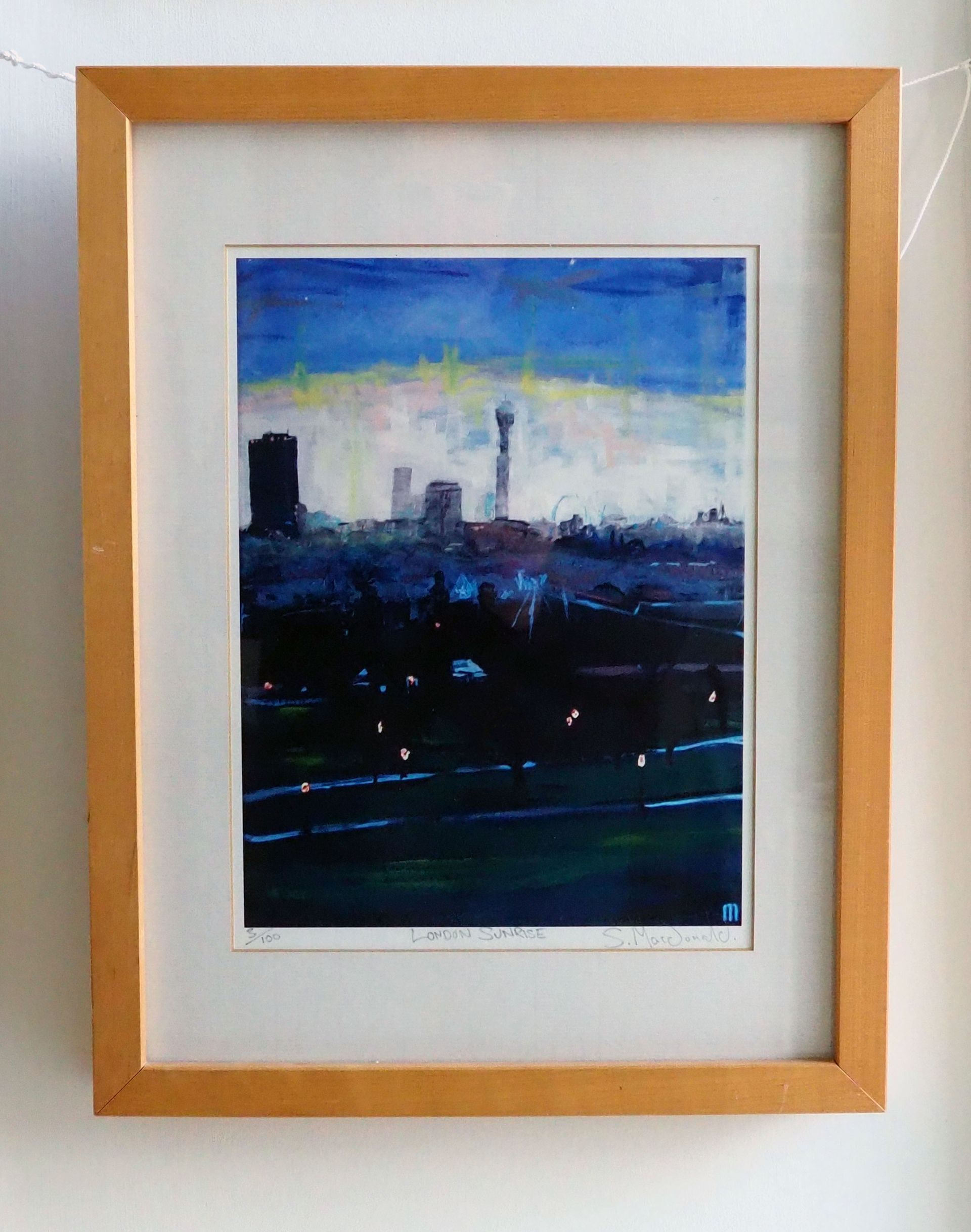 A framed print of painting London Sunrise. A back lit portrait of a city scape with park space in the foreground. The park is still in the dark with its lamp post lights shining orange yellow like fire flies. There are tall grey / lavender purple buildings on the horizon. A white sky surrounds the buildings topped with a yellow layer and then a thick blue and dark blue end of night sky.
