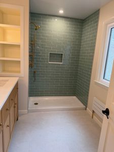Small bathroom with walk-in shower, green tile walls, and white vanity and floor.