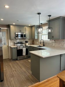 Modern kitchen with gray cabinets, white island countertop, stainless appliances, and wood-look flooring