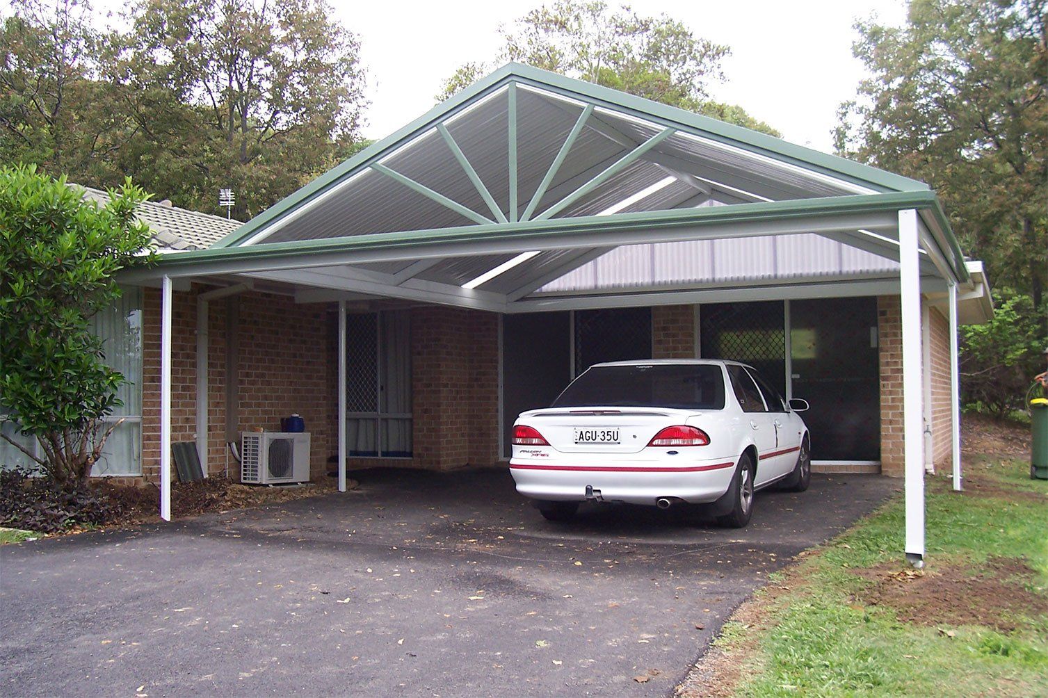 White sedan parked under a green-roofed carport beside a brick house