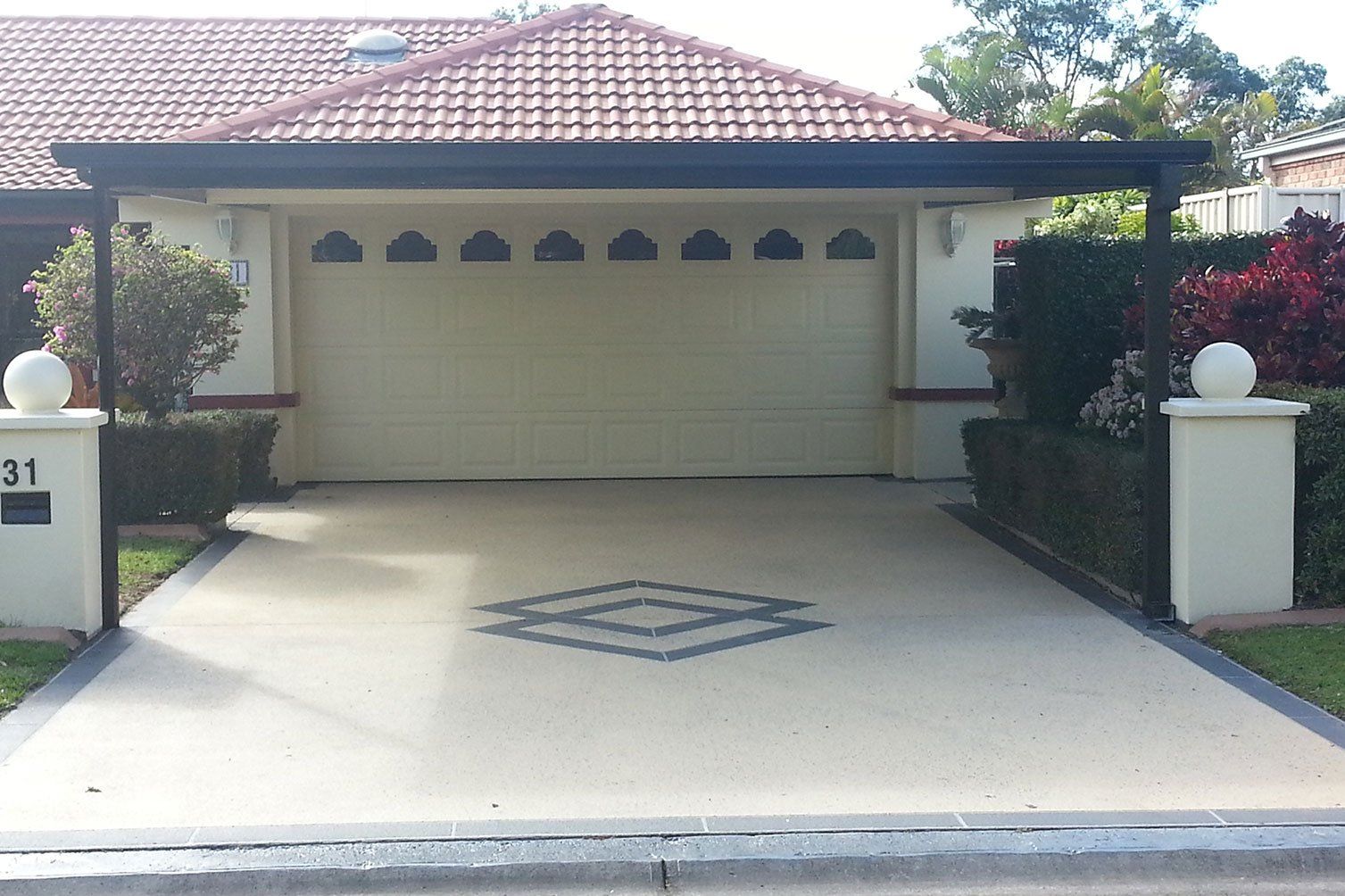 Suburban house with a tiled roof, two-car garage, and concrete driveway, viewed from the street