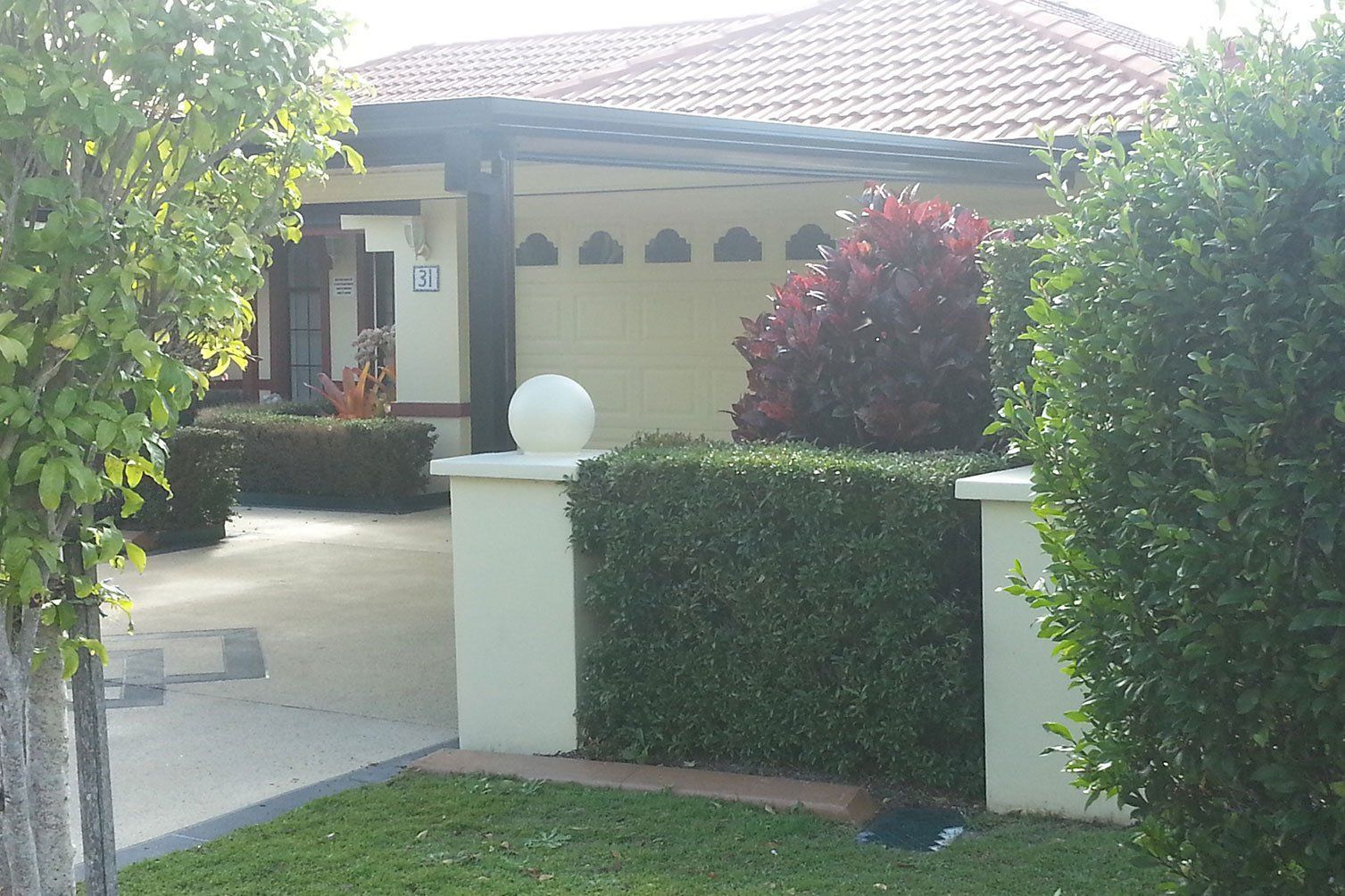 Suburban house with tiled roof, driveway, and neatly trimmed hedges in front yard