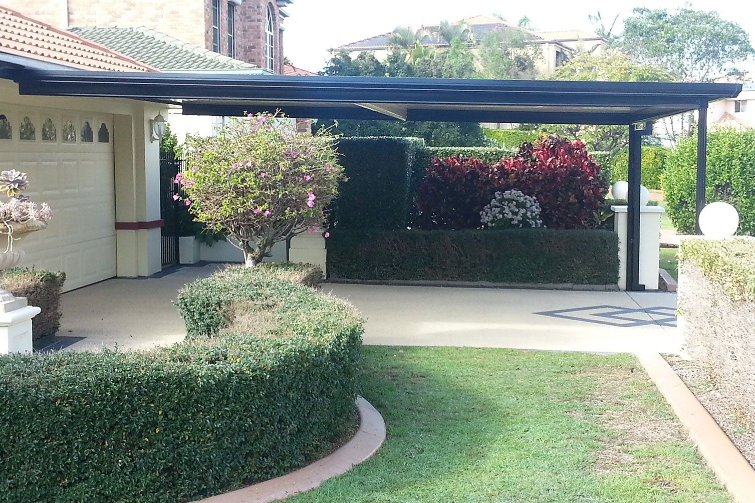 Courtyard garden with hedges, lawn, flowering shrubs, and a covered patio beside a house