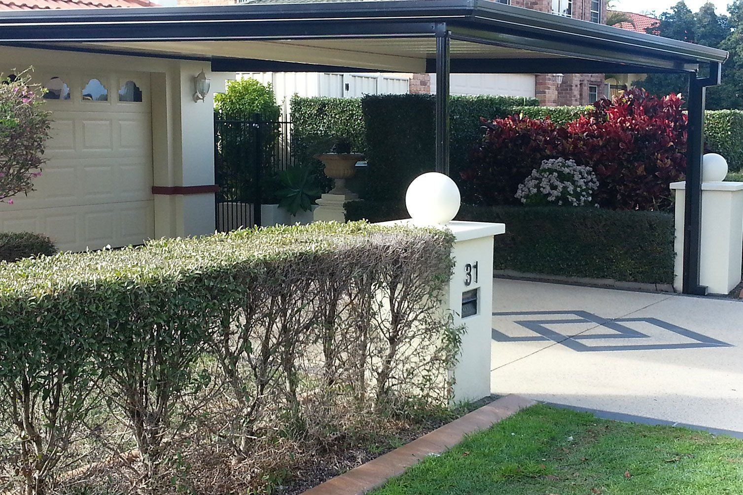 Residential driveway with a carport, trimmed hedges, and a white gate pillar.