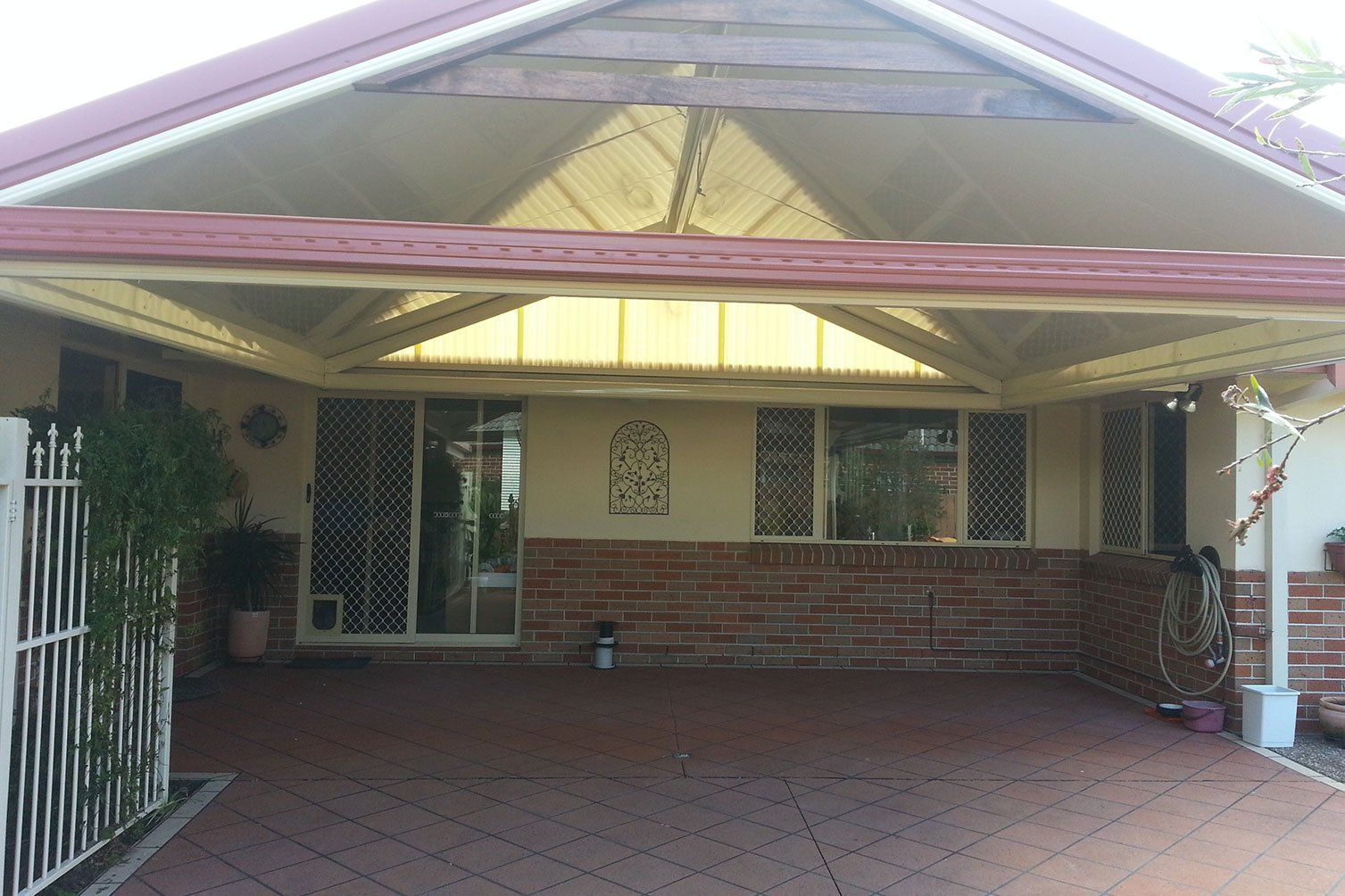 Covered driveway under a pink-trimmed carport with brick paving and house entrance visible