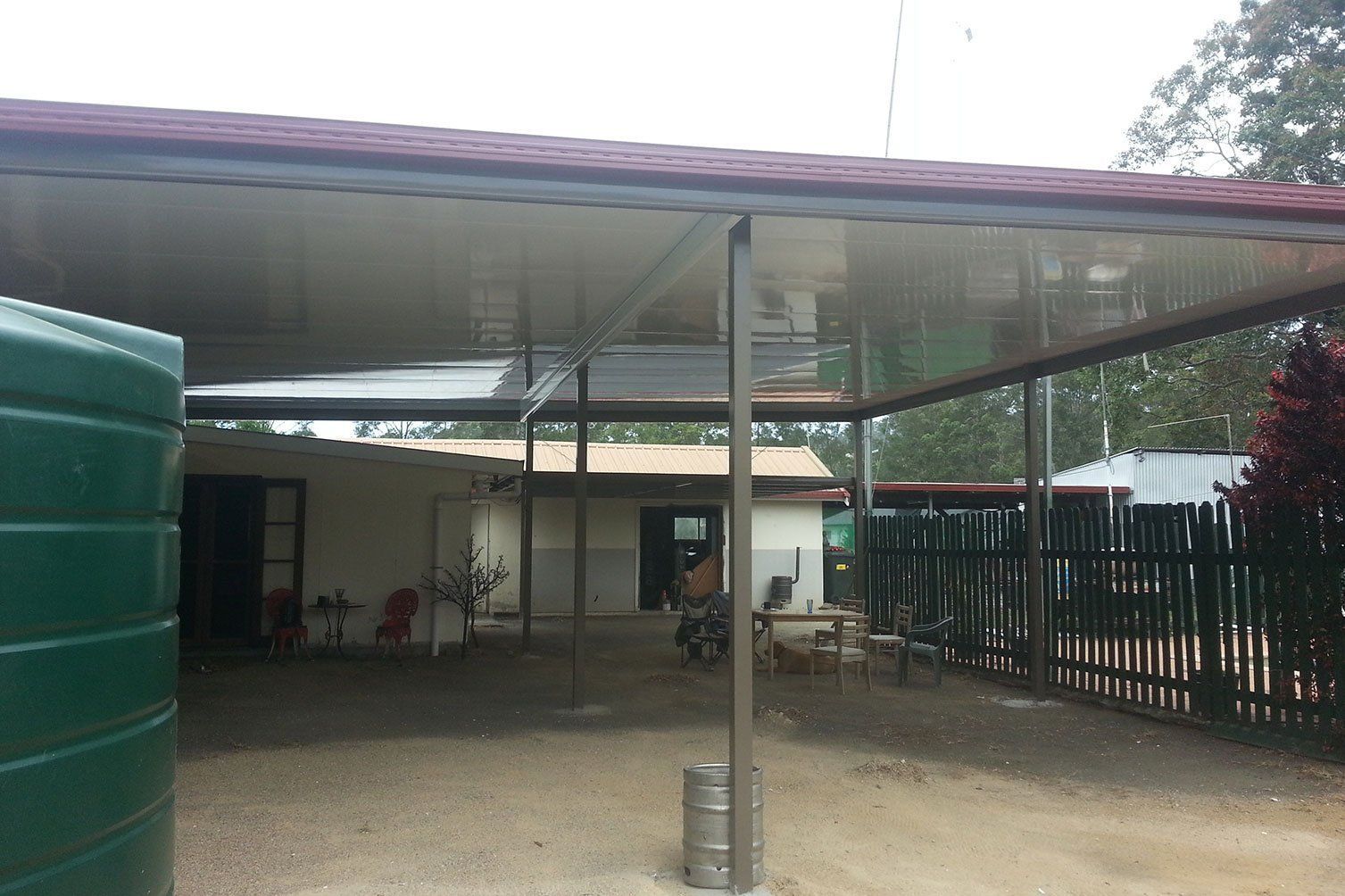 Outdoor covered patio with metal roof, green water tank, and fenced yard area