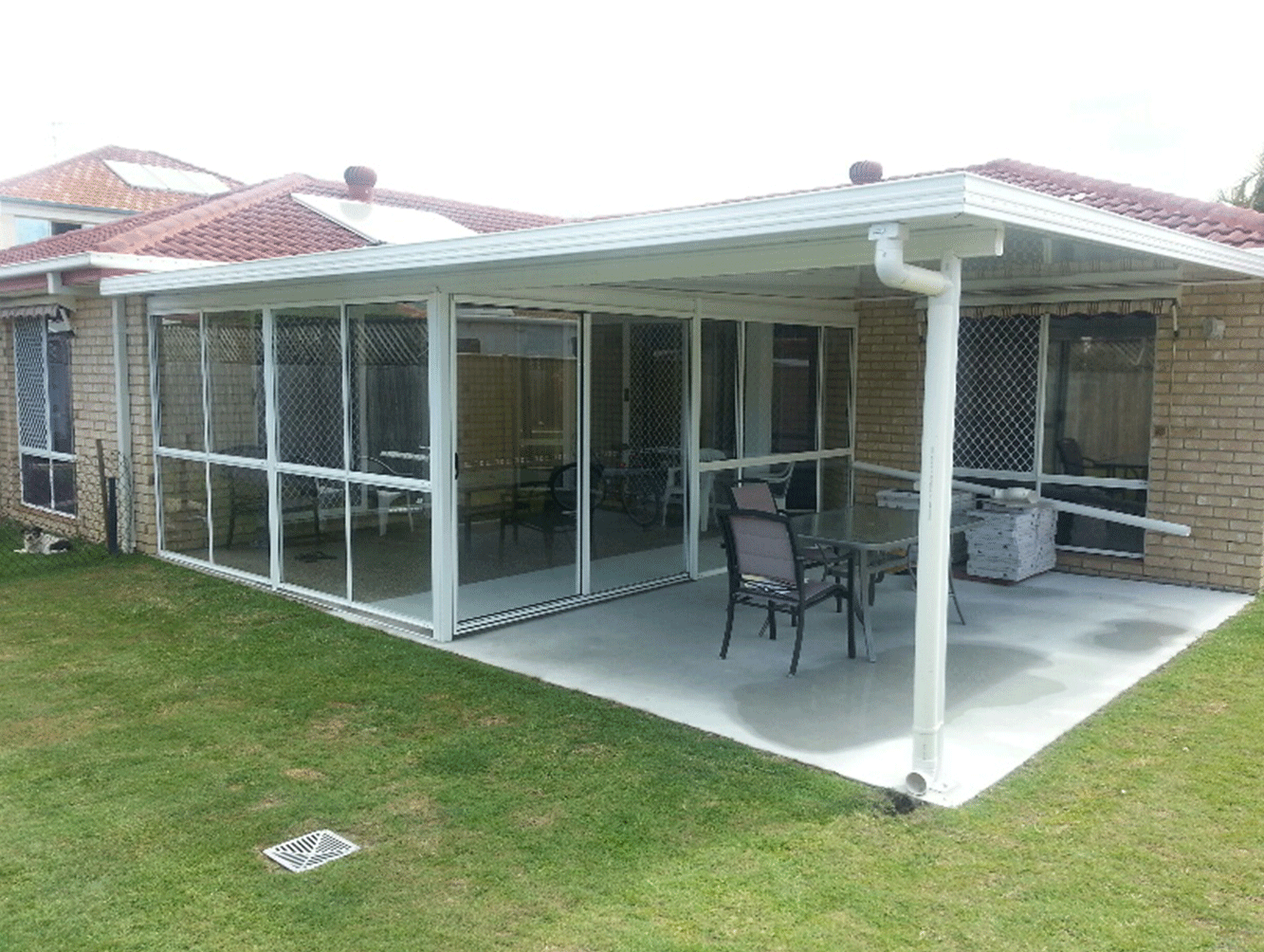 Screened patio with white posts, brick house, patio furniture, and a concrete floor beside a grassy yard.