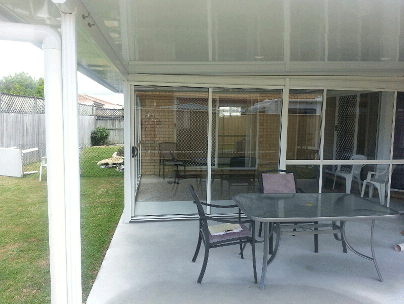 Covered patio with glass table and chairs beside a screened-in porch and grassy yard