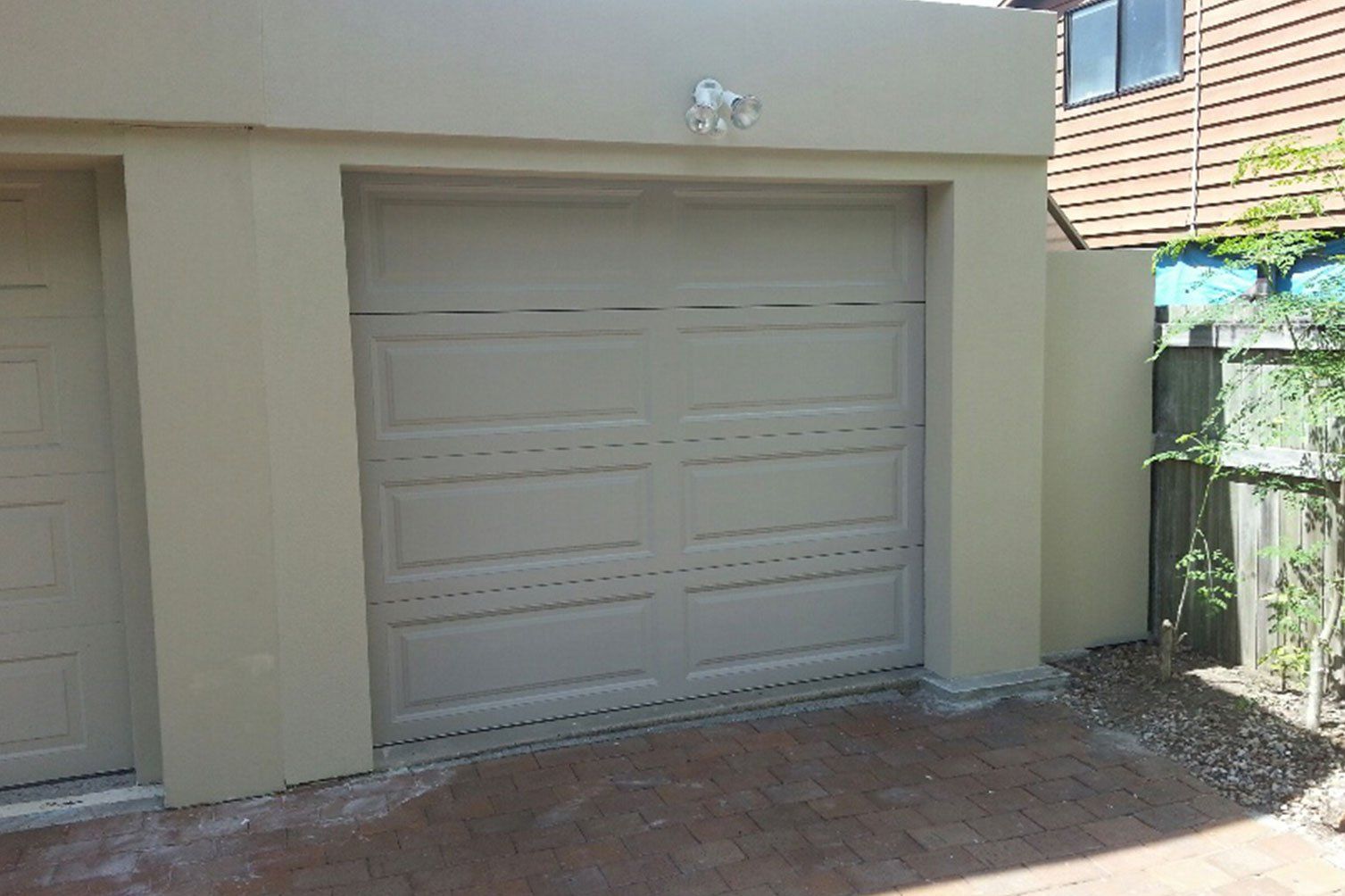 White garage door in a beige exterior wall beside a narrow doorway and brick driveway.