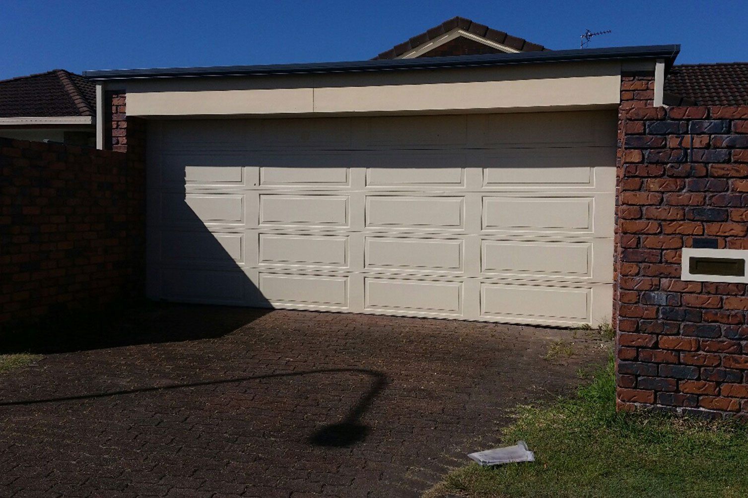 White double garage door on a brick house, with a shadow across the driveway.
