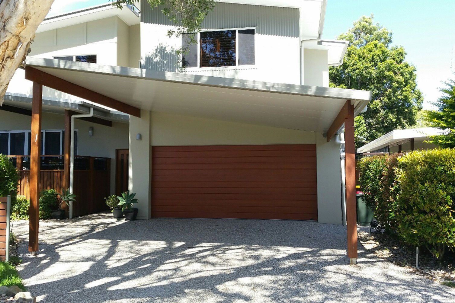 Modern house exterior with a large wooden garage door, slanted carport roof, and gravel driveway