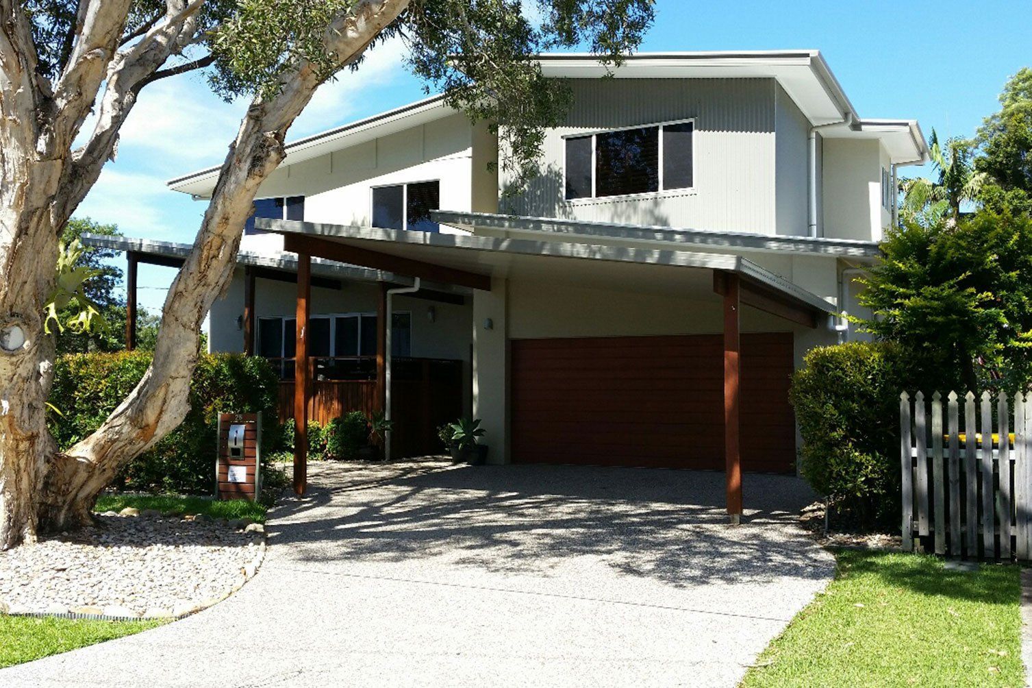 Modern two-story house with carport, sloped roof, tree in front, and gravel driveway