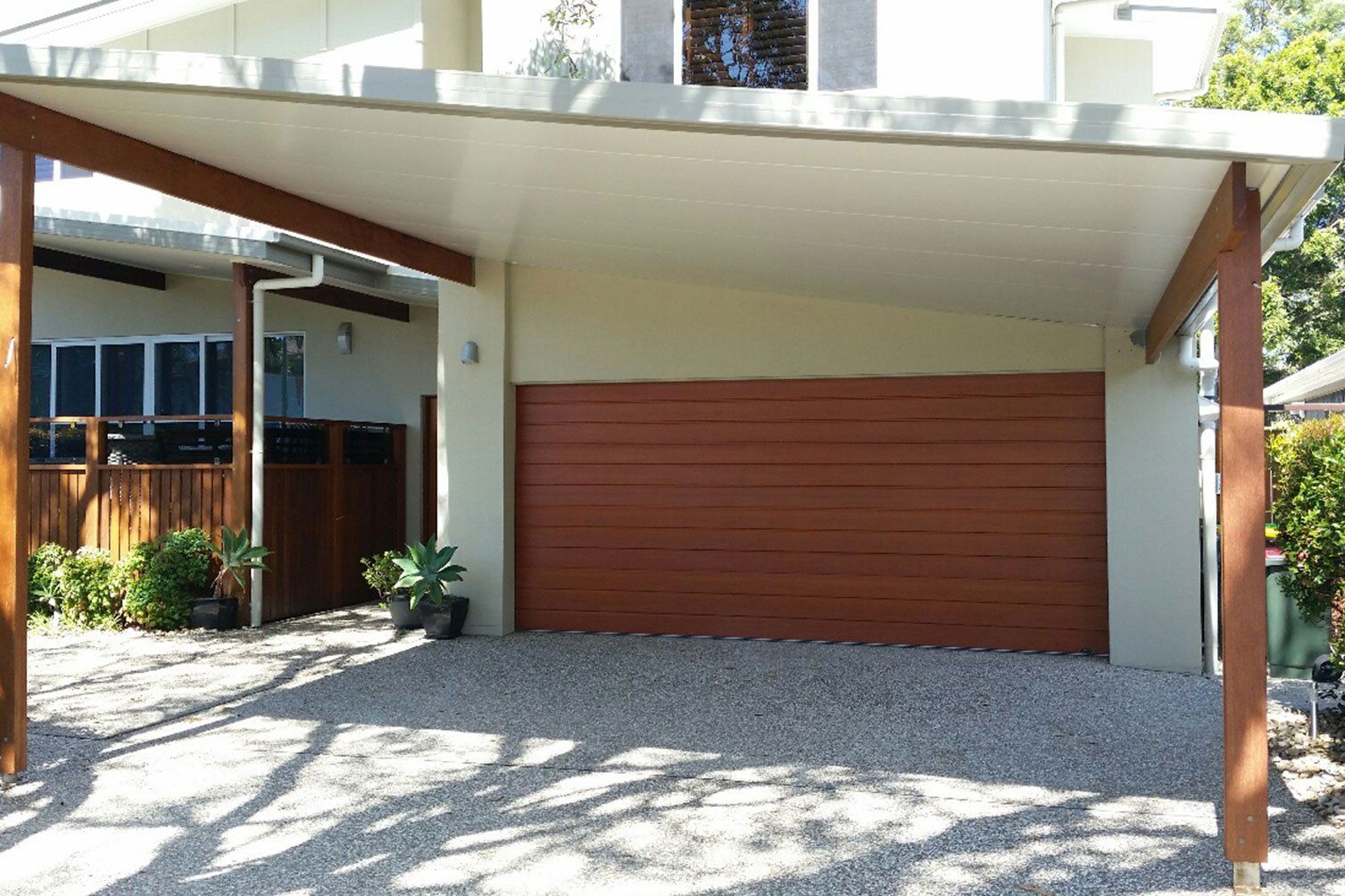 Modern house carport with a large brown garage door and gravel driveway