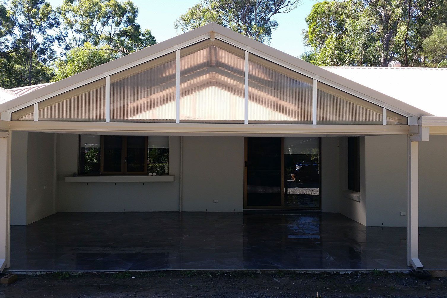 Front view of a gray house with a covered porch and peaked roof, framed by trees.